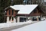 Chalet sous la neige avec bardage en bois brûlé brossé et soubassement en pierre